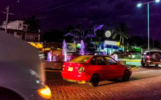 Busy road street driving cars vehicles traffic jam and traffic circle roundabout with dolphin dolphins sculpture statue with fountain at night in Zicatela Puerto Escondido Oaxaca Mexico.