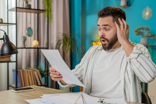 Frustrated shocked amazed business man works at office desk looking at bills paperwork reports documents gets angry frustrated stress bankruptcy financial problem. Stresses freelancer at home