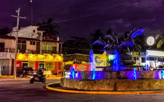 Busy road street driving cars vehicles traffic jam and traffic circle roundabout with dolphin dolphins sculpture statue with fountain at night in Zicatela Puerto Escondido Oaxaca Mexico.