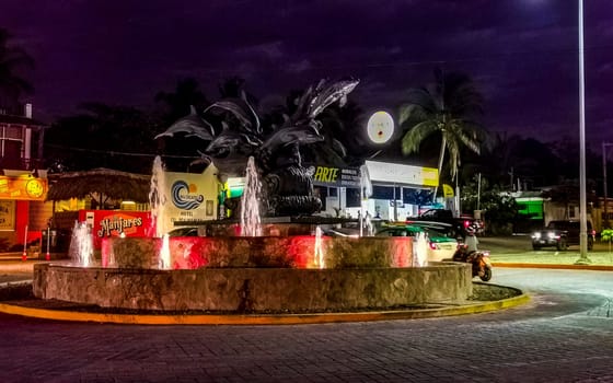 Busy road street driving cars vehicles traffic jam and traffic circle roundabout with dolphin dolphins sculpture statue with fountain at night in Zicatela Puerto Escondido Oaxaca Mexico.