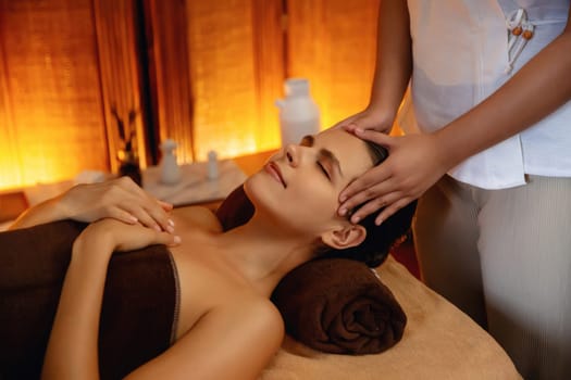 Caucasian woman enjoying relaxing anti-stress head massage and pampering facial beauty skin recreation leisure in warm candle lighting ambient salon spa in luxury resort or hotel. Quiescent