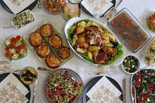 Table full of delicious food in plates, top view. Baked chicken with potatoes, caviar in tartlets, salads, various snacks and drinks at a gala dinner to celebrate the event. Hearty home-cooked food beautifully presented.