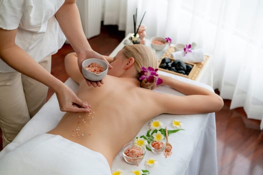 Woman customer having exfoliation treatment in luxury spa salon with warmth candle light ambient. Salt scrub beauty treatment in health spa body scrub. Quiescent