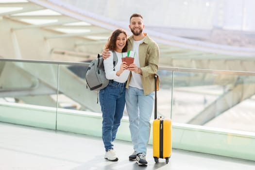 Vacation Trip. Happy Young Spouses With Travel Documents Posing In Airport Terminal, Cheerful Millennial Couple Waiting For Flight, Looking At Camera And Smiling, Enjoying Travelling Together, Free Space