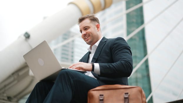 Low angle view of professional business man working on laptop at stairs. Caucasian project manager using computer to plan marketing strategy and communicate with financial team at urban city. Urbane.