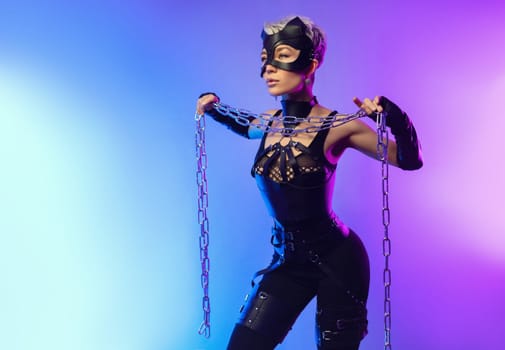 a sexy girl in the erotic image of a catwoman in leather belts and a mask poses against the background of a copy paste in a beautiful neon background with a metal chain in her hands