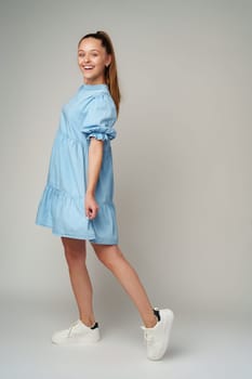 Young happy smiling woman in a light blue dress on a gray background close up