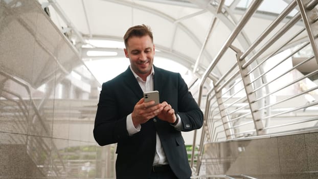 Smart businessman looking or checking his mobile phone while walking at corridor for going to workplace. Happy manager using telephone to send massage to marketing team and receive good news. Urbane.