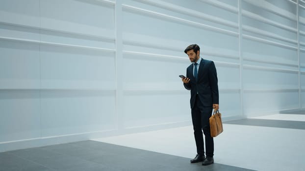 Smart manager looking at phone while standing at white background. Handsome male leader checking email or updated project and planing marketing strategy. while standing at white background. Exultant.