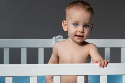 Pensive blue-eyed baby in a white classic crib.
