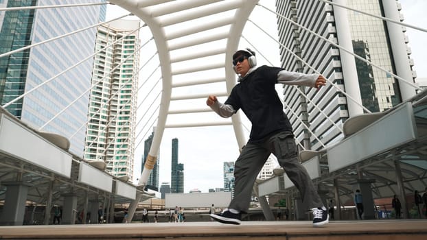 Young asian hipster show footstep at city center surround by people. Stylish fashion street dancer perform B-boy or freestyle dancing with low angle. Outdoor sport 2024. Break dancing. Sprightly.