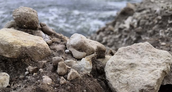 A rock formation stands prominently on the sandy beach, with the vast body of water stretching out in the background. The waves gently crash against the shore under a clear sky.