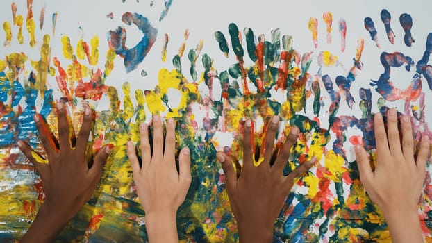 Happy diverse student hand placed on colorful stained wall. Closeup of multicultural hand or children with mixed races paint their hand print at art room. Background. Creative activity. Edification.