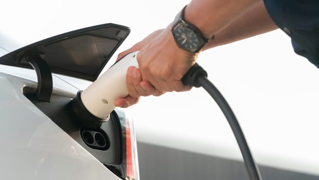 Closeup hand put EV charger to recharge electric car's battery from charging station in city commercial parking lot. Rechargeable EV car for sustainable environmental friendly urban travel. Expedient