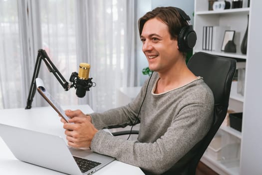 Host channel in smart broadcaster with talking show on live social media streaming with script note reading to listeners, wearing headphones to record video streamer at modern home studio. Pecuniary.