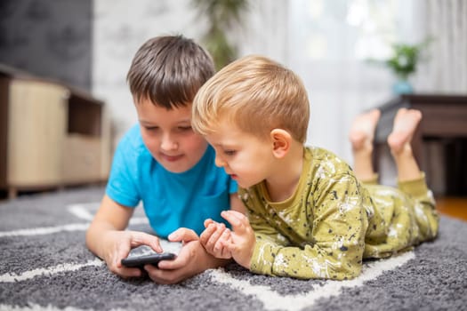 Two young boys lying on carpet using smartphone together. Indoor leisure, digital childhood, and brotherhood concept for design and print