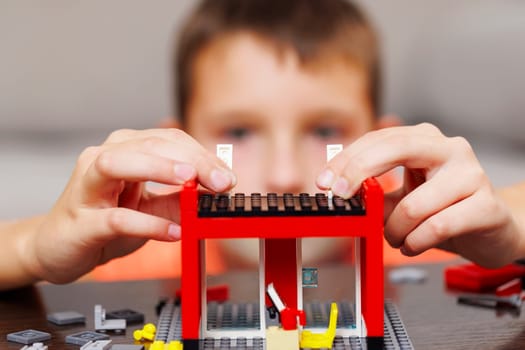 Child building a red toy structure with blocks on a table. Creative play and learning concept. Design for educational poster, children's toy advertisement