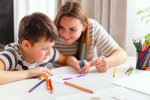 Mother and son drawing together with colorful pencils. Indoor leisure activity and family bonding concept with copy space for design and print