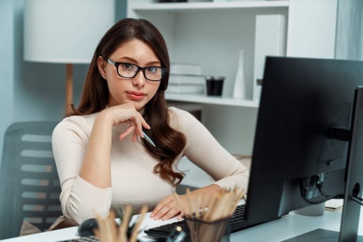 Portrait casual outfit smiling beautiful woman looking camera to pose for business profile while working on desk surrounded pc and stationary theme of positive new generation modern office. Postulate.