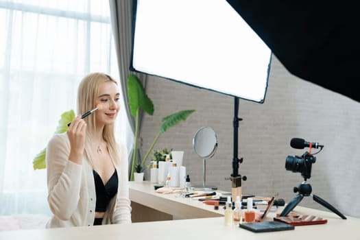 Young woman making beauty and cosmetic tutorial video content for social media. Beauty blogger smiles to camera while showing how to beauty care to audience or followers. Blithe