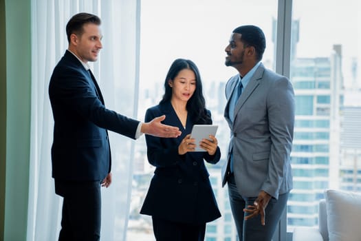 Diverse smart businesspeople standing near window with skyscraper while looking at business data analysis. Group of business team using tablet represent marketing plan, strategy, idea. Ornamented..