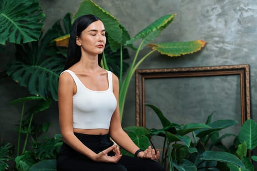 Young woman doing morning yoga and meditation in natural garden with plant leaf, enjoying the solitude and practicing meditative poses. Mindfulness activity and healthy mind lifestyle. Blithe