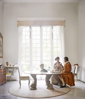 King, queen and royal couple with tea in castle, smile and talk in vintage clothes with luxury at breakfast. Woman, man and people with drink in morning with Victorian fashion at regal palace in UK.