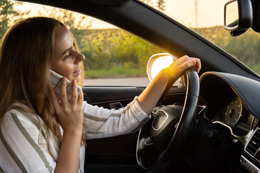 Young woman using mobile phone while driving car on highway road during sunset. Womandriver has accident calling with smartphone for help. Business woman busy driving concept