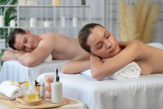 Blissful couple customer having exfoliation treatment in luxury spa salon with warmth candle light ambient. Salt scrub beauty treatment in health spa body scrub. Quiescent