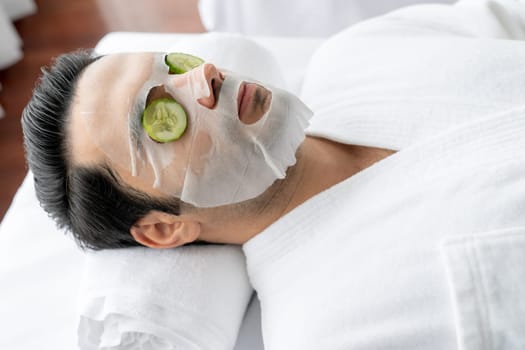 Serene daylight ambiance of spa salon, man customer indulges in rejuvenating with luxurious cucumber facial mask. Facial skincare treatment and beauty care concept. Quiescent