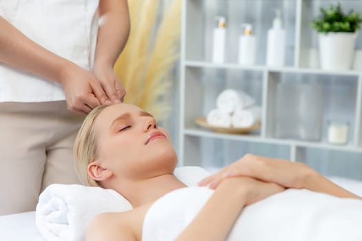 Caucasian woman enjoying relaxing anti-stress head massage and pampering facial beauty skin recreation leisure in dayspa modern light ambient at luxury resort or hotel spa salon. Quiescent