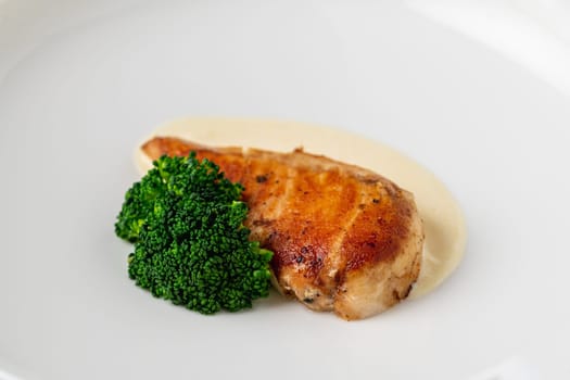 Grilled chicken breast with broccoli and sauce on a white porcelain plate