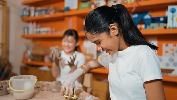 Happy multicultural girl and friend put the clay on the each other muddy shirt at art lesson. Diverse highschool student playing with clay at pottery workshop. Creative activity concept. Edification.