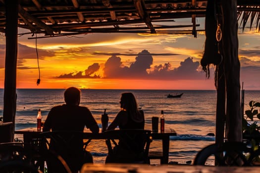 A couple drinks wine in a cafe against the backdrop of a sunset at sea. Silhouettes of people.