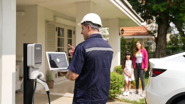 Qualified technician working on home EV charging station installation, making troubleshooting and configuration setup on charging system with empty laptop screem for EV at home. Synchronos