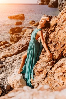 Woman green dress sea. Woman in a long mint dress posing on a beach with rocks on sunny day. Girl on the nature on blue sky background