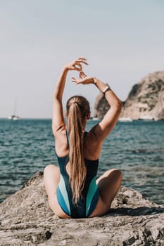 Yoga on the beach. A happy woman meditating in a yoga pose on the beach, surrounded by the ocean and rock mountains, promoting a healthy lifestyle outdoors in nature, and inspiring fitness concept