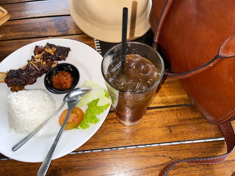 Spicy hot honey roasted grilled spare ribs served with hot chili paste on wooden table and rice also ice tea served in white plate