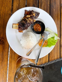 Spicy hot honey roasted grilled spare ribs served with hot chili paste on wooden table and rice also ice tea served in white plate