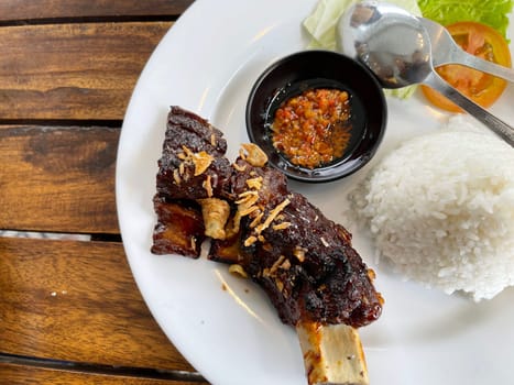 Spicy hot honey roasted grilled spare ribs served with hot chili paste on wooden table and rice also ice tea served in white plate