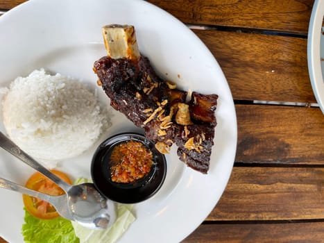 Spicy hot honey roasted grilled spare ribs served with hot chili paste on wooden table and rice also ice tea served in white plate