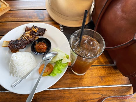 Spicy hot honey roasted grilled spare ribs served with hot chili paste on wooden table and rice also ice tea served in white plate