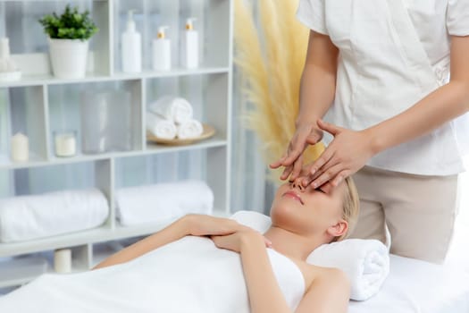 Caucasian woman enjoying relaxing anti-stress head massage and pampering facial beauty skin recreation leisure in dayspa modern light ambient at luxury resort or hotel spa salon. Quiescent