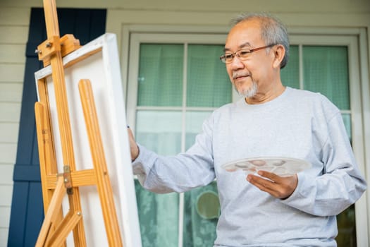 Artist. Asian senior old man painting picture using brush and oil color on canvas, lifestyle elderly people smile paint at his easel, Happy retirement and activity concept