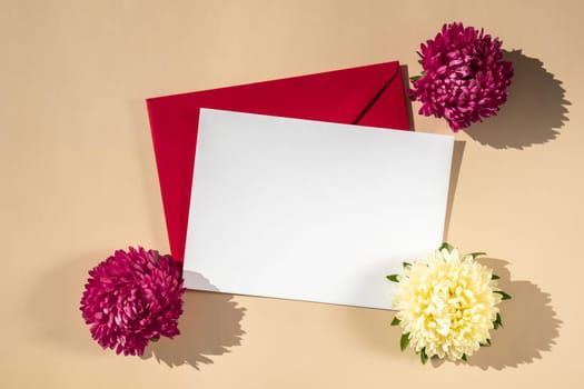 Composition with empty paper note and envelope beautiful spring red and white flowers on beige background. Mockup card invitation greeting card postcard copy space template. Blooming fresh natural flower.