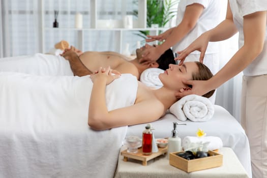 Caucasian couple enjoying relaxing anti-stress head massage and pampering facial beauty skin recreation leisure in dayspa modern light ambient at luxury resort or hotel spa salon. Quiescent