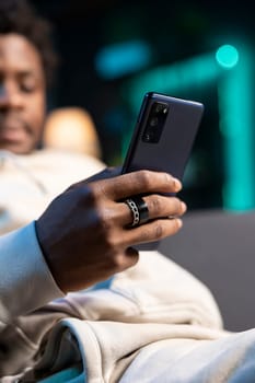 Close up shot on smartphone held by person texting internet friends, enjoying himself at home. Focus on phone used by african american man in blurry background to enjoy leisure time