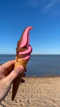 Ice cream in cone melting in sun in hand against backdrop of beach by the sea, vertical photo of travel concept