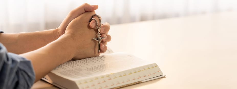 Asian male folded hand prayed on holy bible book while holding up a pendant crucifix. Spiritual, religion, faith, worship, christian and blessing of god concept. Blurring background. Burgeoning.