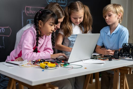 Skilled kids learning to program remote car. Schoolgirl in pink cloth use laptop for coding. Other child watch her code while teacher watch her. motherboard and electric wire also on table. Erudition.